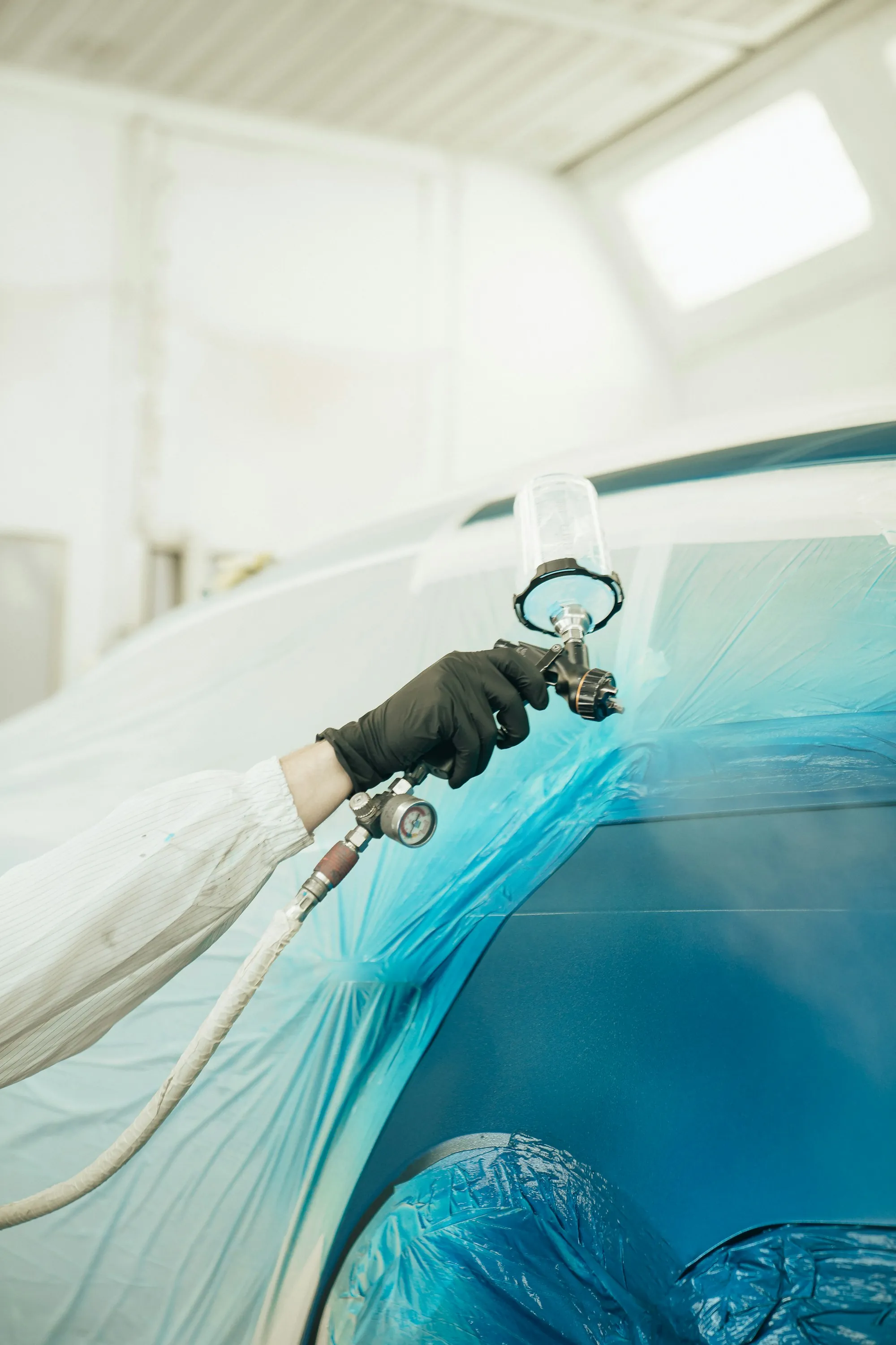 Painter in protective gear spraying a car body panel in a paint booth