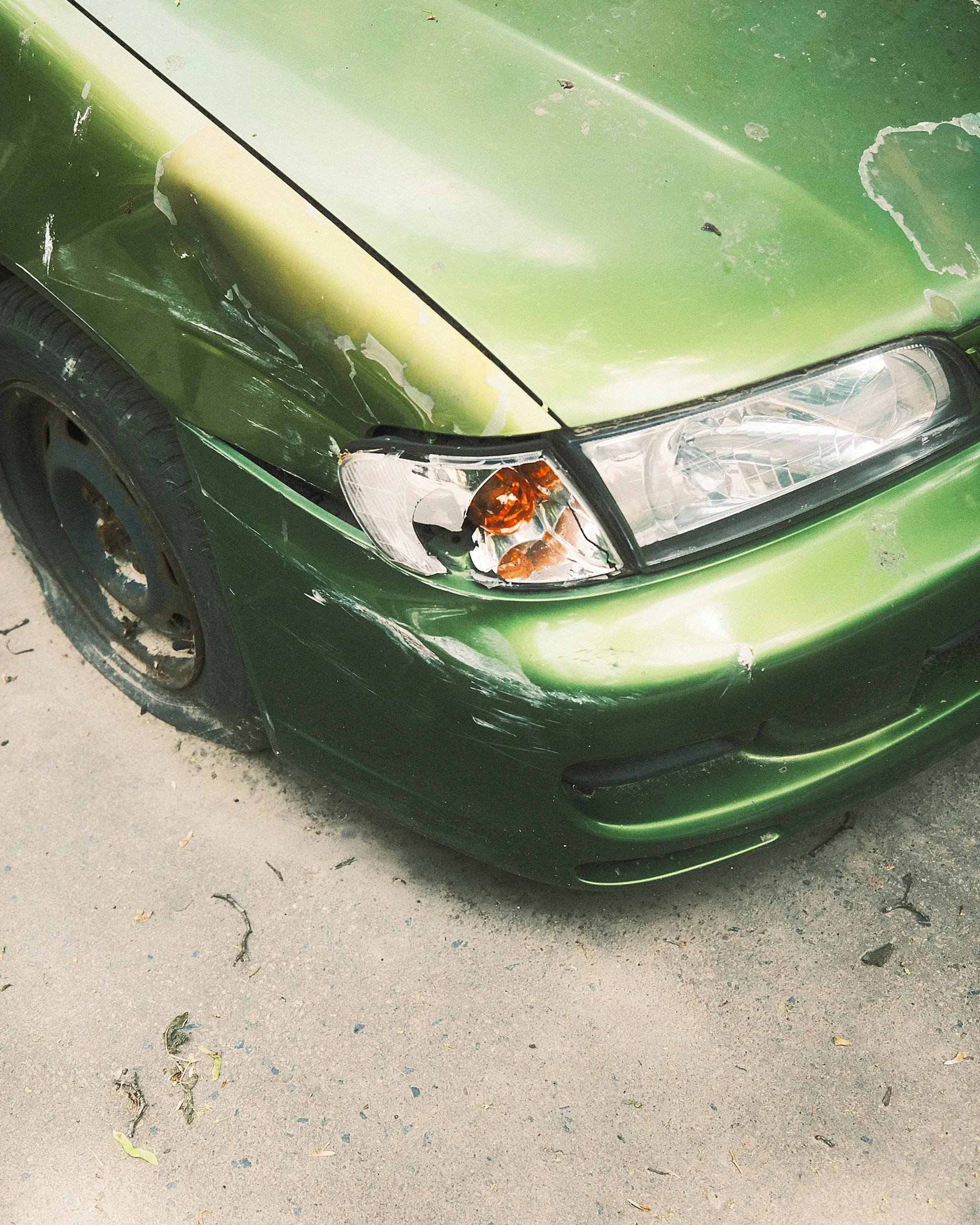 Green car with a dented and cracked front bumper