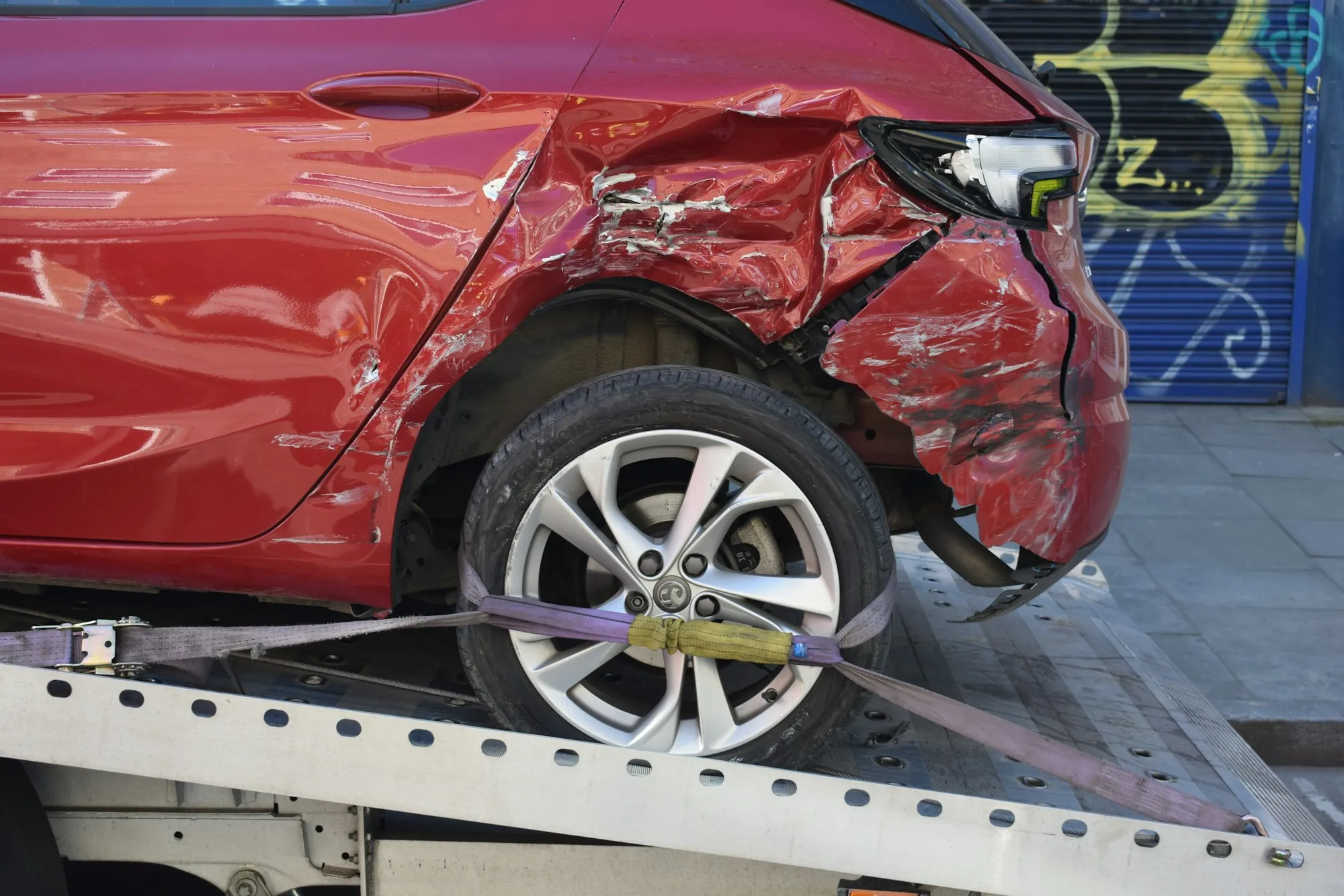 Red car with heavy front-end damage loaded on a flatbed tow truck
