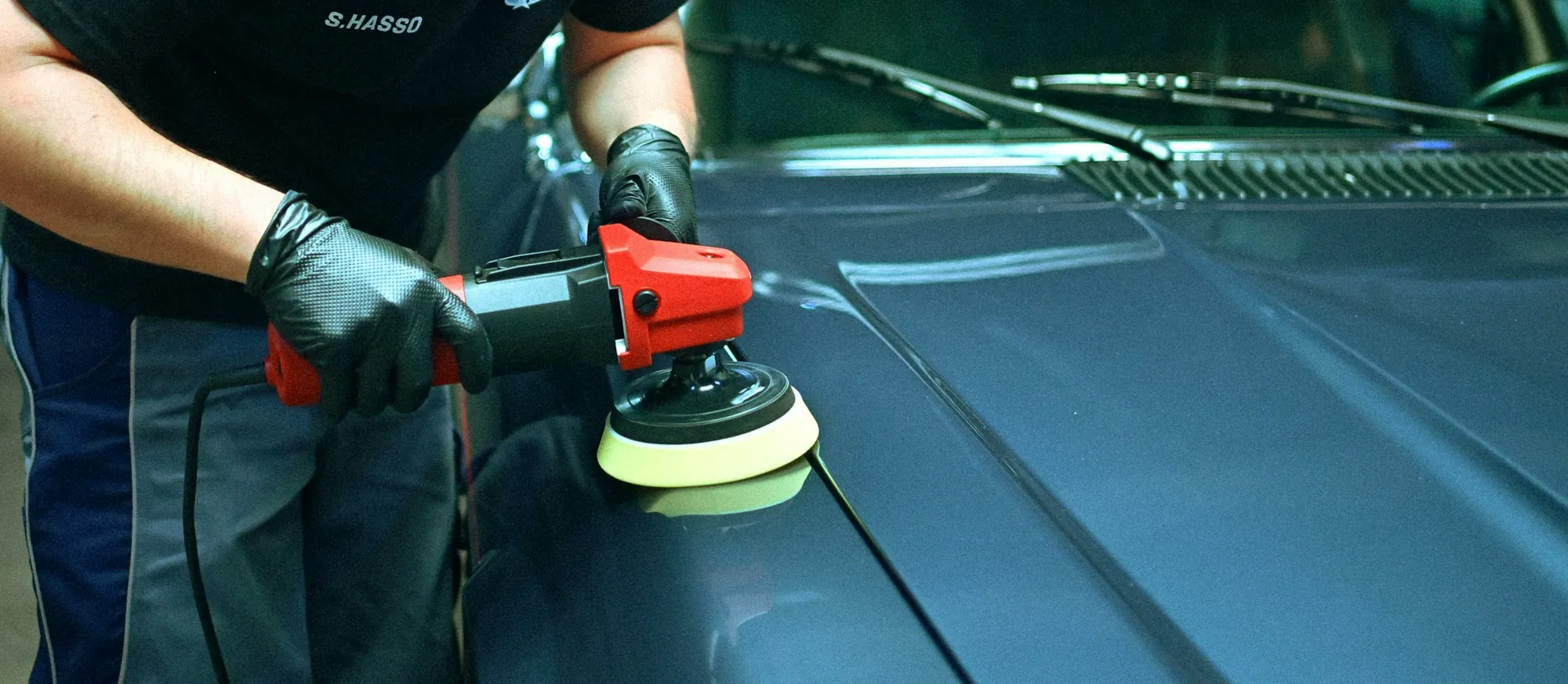 Technician polishing a blue car's hood with an orbital buffer