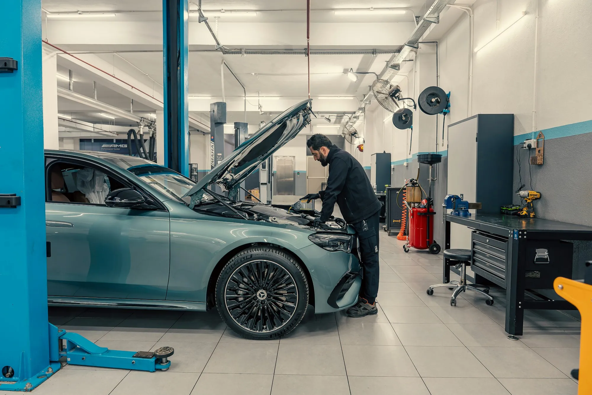 Mechanic inspecting the underside and engine area of a car in a repair bay