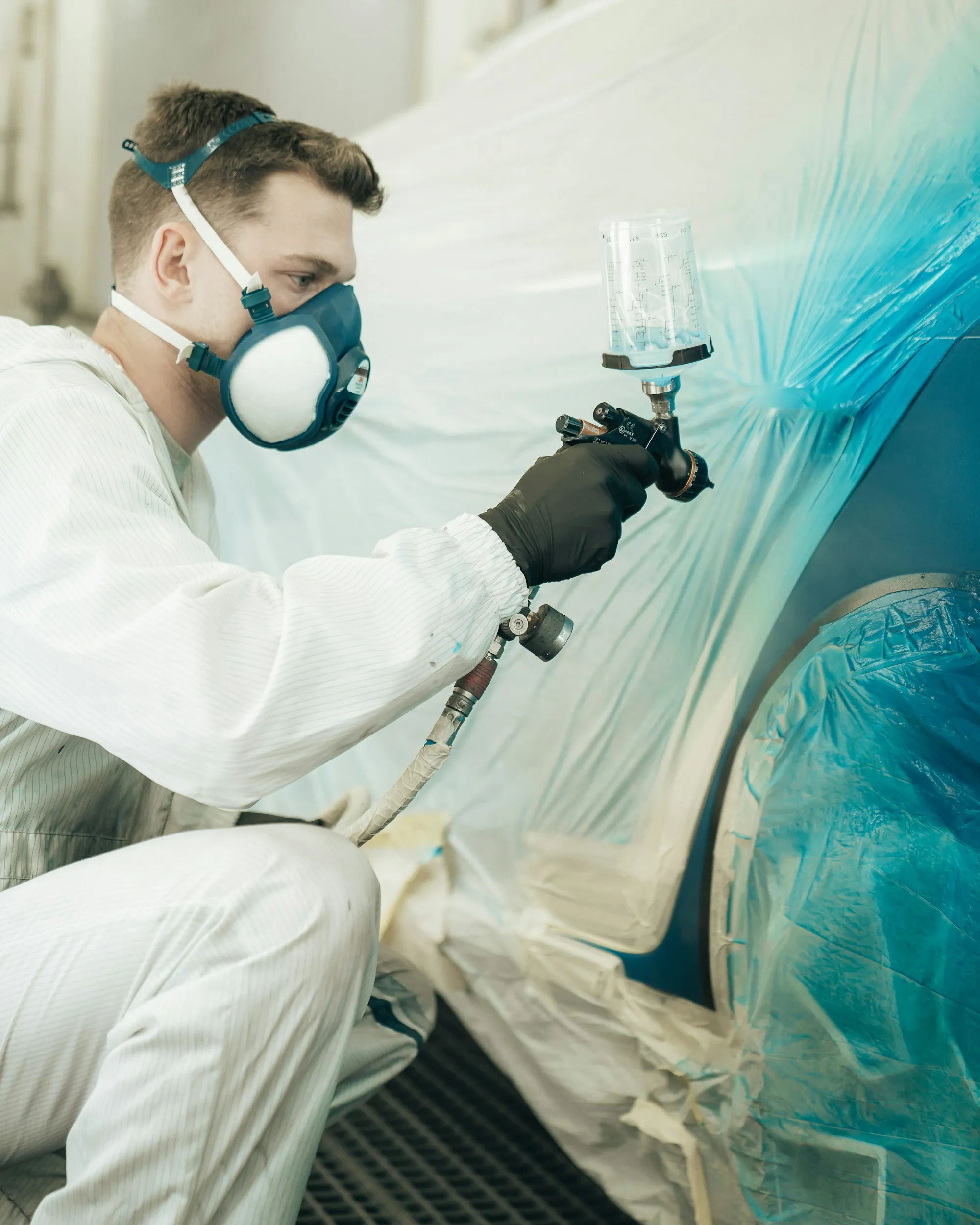Painter in protective gear spraying a car panel