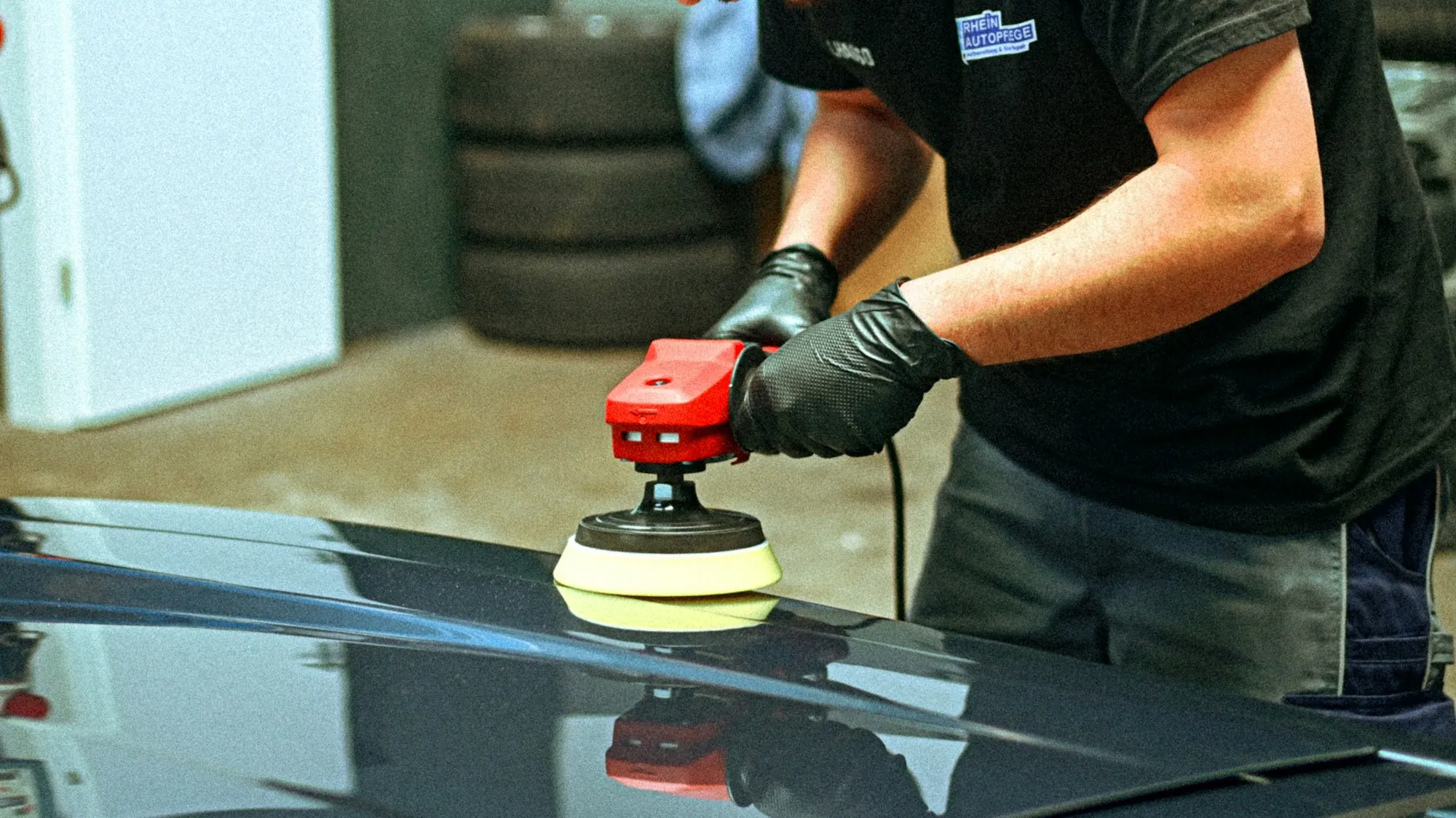 Close-up of a technician polishing the glossy paint of a dark car