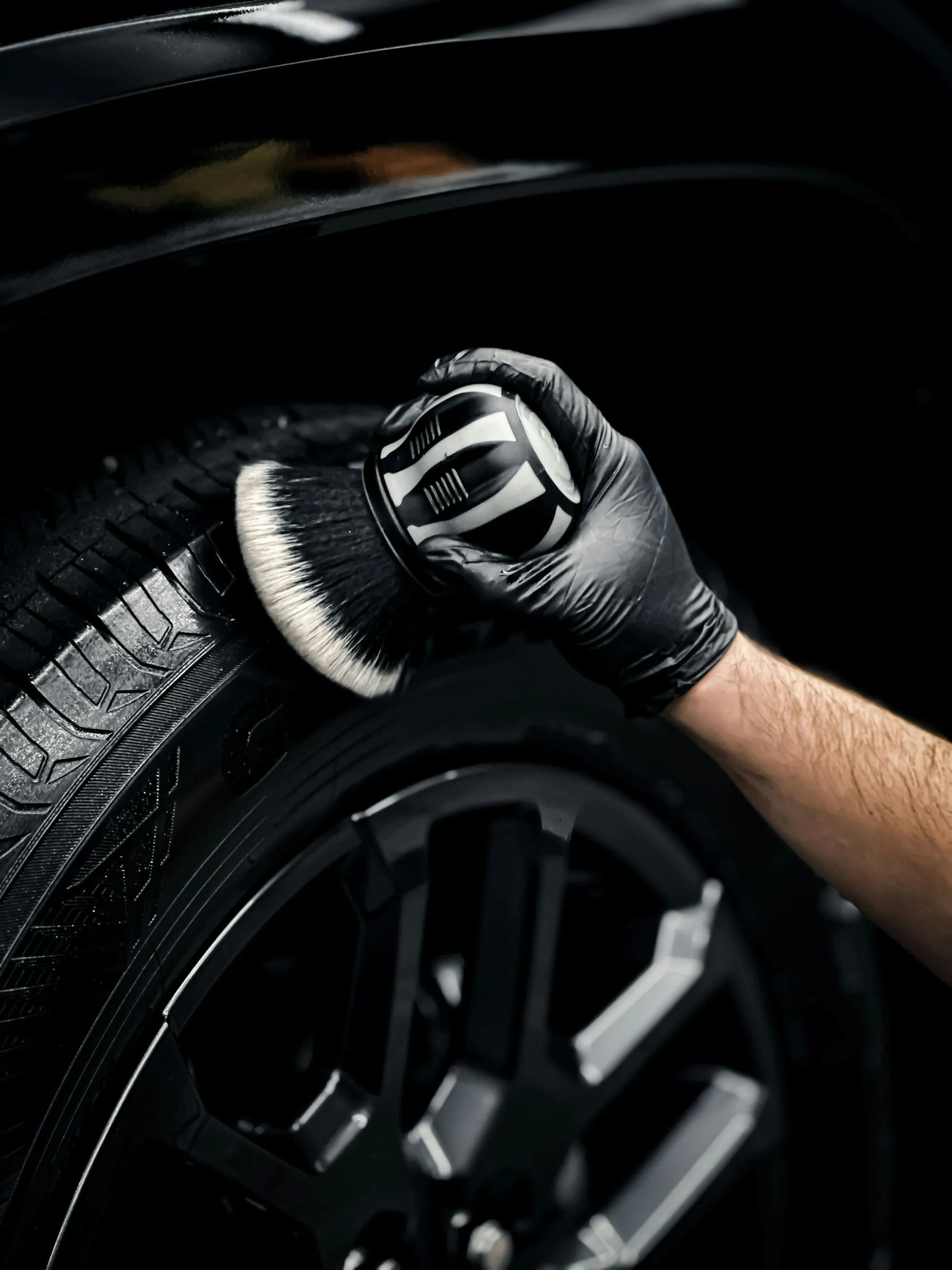 Gloved hand cleaning a car wheel with a brush